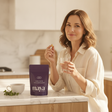 Woman taking Maya GUT+ with water in a bright morning kitchen
